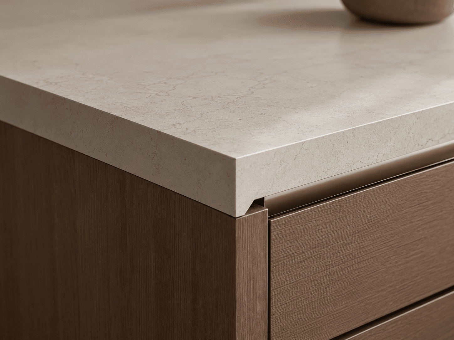 45° meeting between light stone counter and Ookora walnut front with integrated brushed brass linear pull.